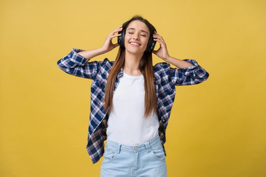 Beautiful calm young woman listening the music in headphone with closed eyes on yellow background. Closeup