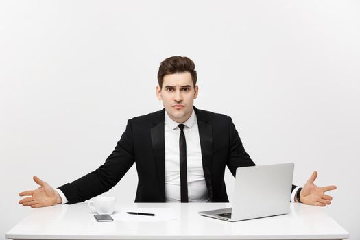 Business Concept: Young businessman working in bright office, sitting at desk, using laptop with serious facial expression