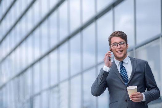 young businessman with coffee talking on smartphone