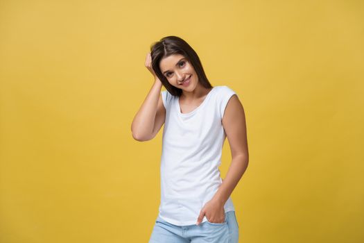 Smiling beautiful young woman in white shirt looking to camera. Three quarter length studio shot on yellow background.