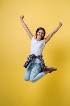 Full-length portrait of carefree girl in white shirt and jean jumping on yellow background.