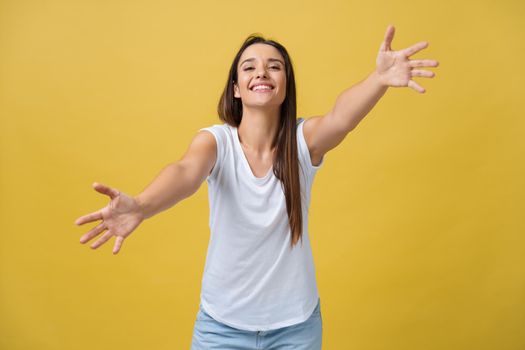Closeup portrait, young, happy, smiling woman, motioning with arms to come, give her bear hug, isolated yellow background. Positive human emotion facial expression feeling, sign symbol, body language