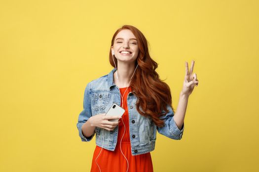 Liftstyle: Portrait of a pretty smiling caucasian woman in headphones listening to music and showing peace gesture isolated over yellow background