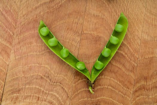 One opened stitch of peas, with grains of peas on a wooden board