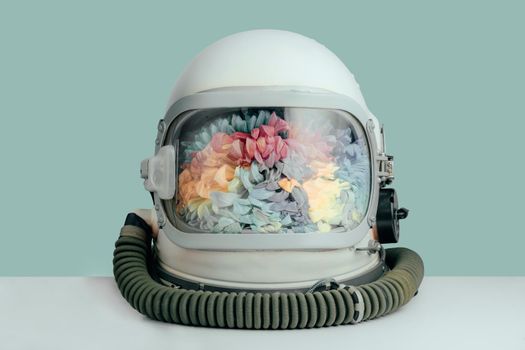 Closed astronaut helmet filled with colorful chrysanthemum flowers on mint color background. Cosmonaut space helmet with flowers