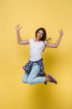 Full-length portrait of carefree girl in white shirt and jean jumping on yellow background.