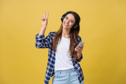 Lifestyle Concept - Portrait of beautiful caucasian woman joyful listening to music on mobile phone. Yellow pastel studio background. Copy Space.