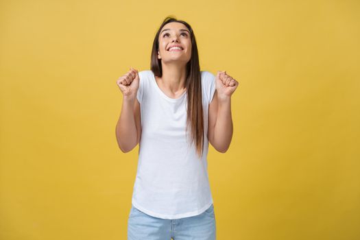 Surprised young woman in excited emotion over yellow background. Looking at camera