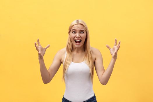 Portrait of an angry irritated woman with hands raised shouting at camera isolated on yellow background