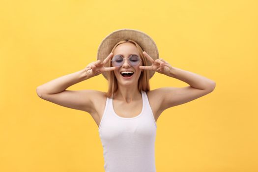 Image of cheerful caucasian woman wearing casual clothing smiling and showing peace sign with two fingers isolated over yellow background in studio.