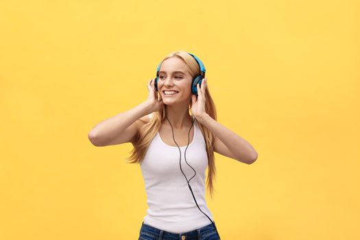 Happy girl dancing and listening to the music isolated on a yellow background