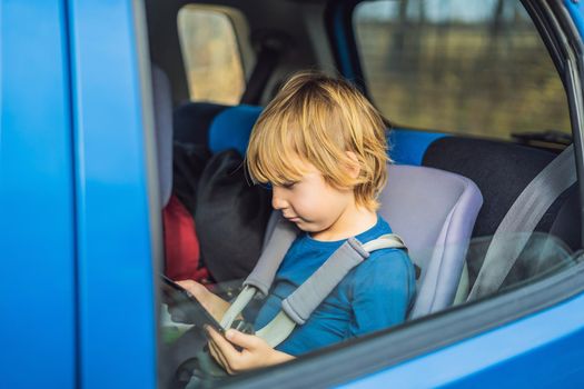 Little boy traveling on backseat of a car using touch pad to entertain himself during the trip