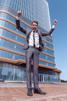 in full growth. a jubilant businessman standing in front of a tall office building.