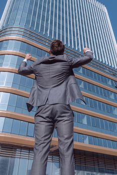 rear view. happy businessman standing in front of tall office building.