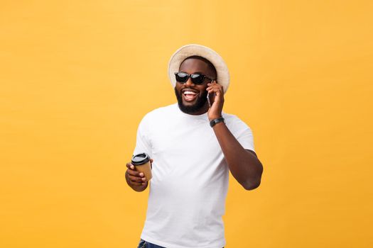 Handsome African American with mobile phone and take away coffee cup. Isolated over yellow gold background.