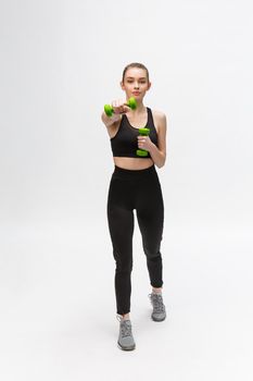 Portrait of Caucasian woman on white background wearing black fitness separate and excercising with dumbells.