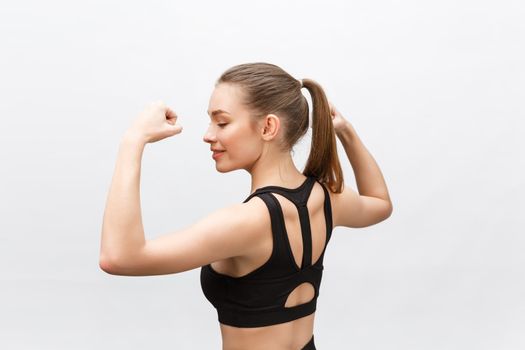 Waist up shot of sporty woman raises hand to show her muscles, feels confident in victory, looks stong and independent, smiles positively, stands against grey background. Sport concept