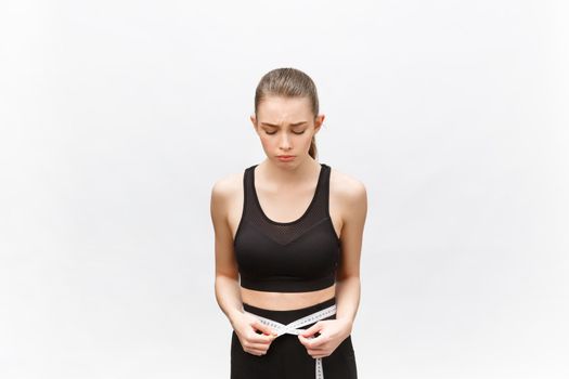 Young woman with excess weight in sporty top sadly looking on result of measuring waist over white background