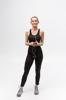 Sport woman. Young beautiful woman in sport clothes. Portrait full length sitting in headphones listening music.