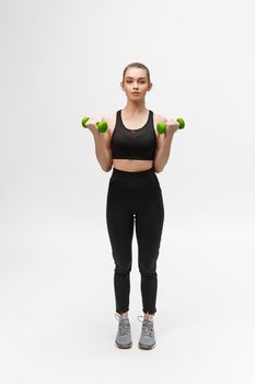 Portrait of Caucasian woman on white background wearing black fitness separate and excercising with dumbells.