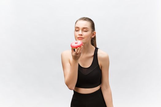 Beautiful Fitness model wearing a black fitness outfit holding a junk food donut. Isolated over grey background.