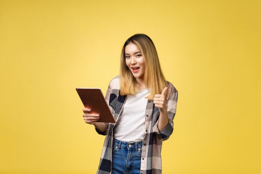 Asian woman use of tablet pc and thumb up isolate on yello background.