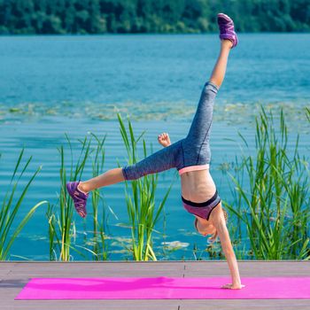 Cute girl doing acrobatic handstand by the lake