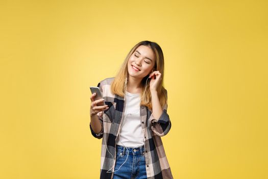 Fashion smiling asian woman listening to music in earphones over yellow background.