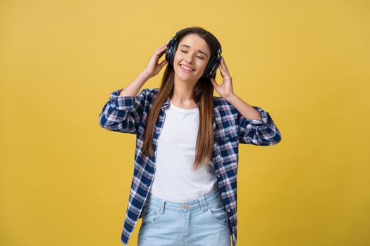 Beautiful calm young woman listening the music in headphone with closed eyes on yellow background. Closeup