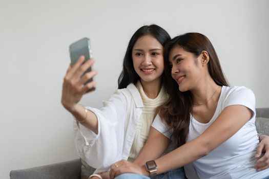 Asian beautiful lesbian or friends using mobile phone to take selfie together on couch. LGBT, Technology and Lifestyle Concept
