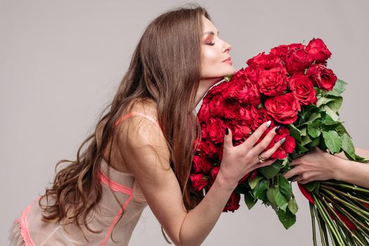 Gorgeous brunette woman in night gown smelling red roses.