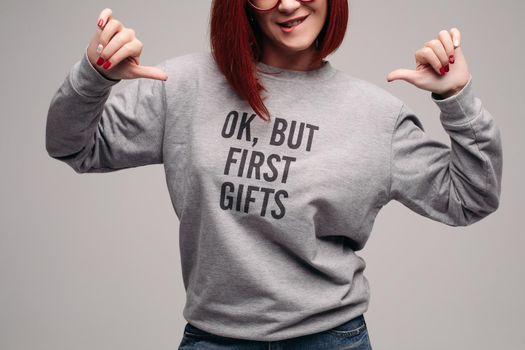 Red haired girl wearing gray sweatshirt showing her look, waiting for presents.