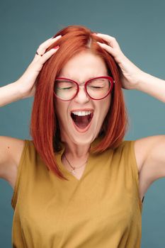 Happy and positivity red haired woman in eyeglasses shouting holding head by hands.