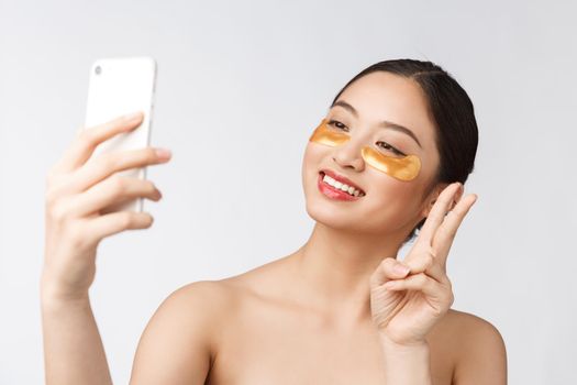 Close up selfie of beautiful happy woman with eye mask on face.Woman with eyes mask taking selfie with mobile phone at home enjoying relaxation and