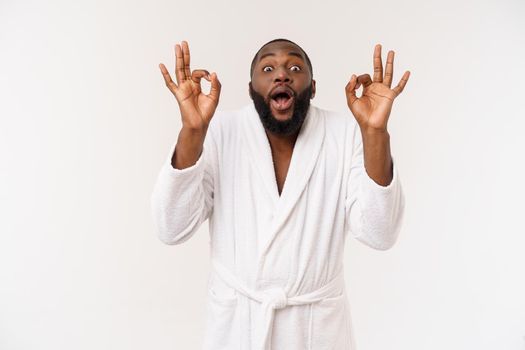 Young African man in bathrobe prepare for skin care showing ok finger sign. Human emotions concept