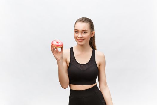 Beautiful Fitness model wearing a black fitness outfit holding a junk food donut. Isolated over grey background.