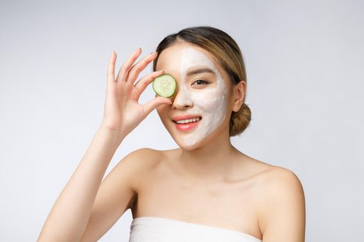 Asian young beautiful smiling woman with flawless complexion holding cucumber slices over eye.