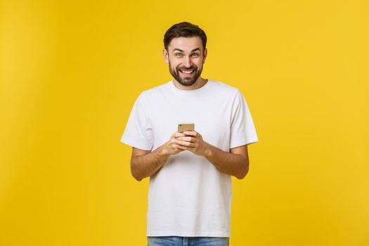 Good news from friend. Confident young handsome man in jeans shirt holding smart phone against yellow background
