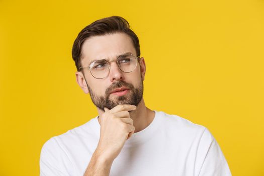 Thinking man isolated on yellow background. Closeup portrait of a casual young pensive man looking up at copyspace. Caucasian male model.