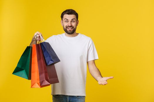 Photo of happy guy, holding shopping bags, isolated over yellow background