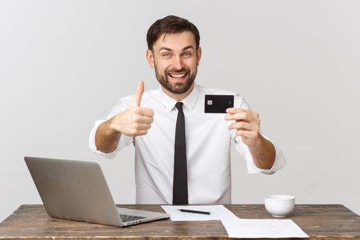 Image of cheerful businessman in suit smiling while holding laptop and credit card isolated over gray background.