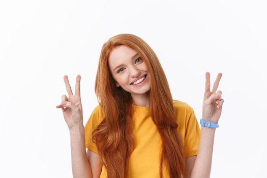Portrait of cheerful young woman showing two fingers or victory gesture, over grey background.