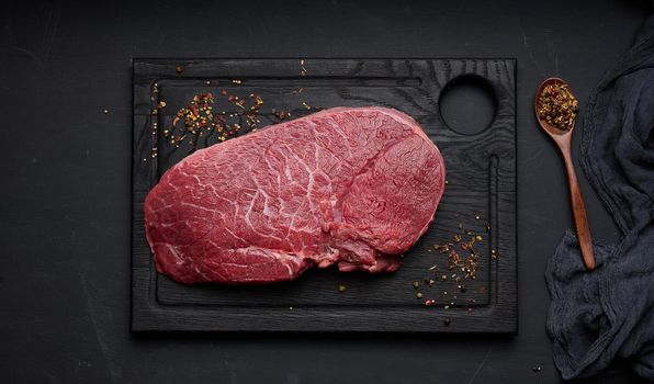 Raw beef tenderloin lies on a wooden cutting board on a black table, top view