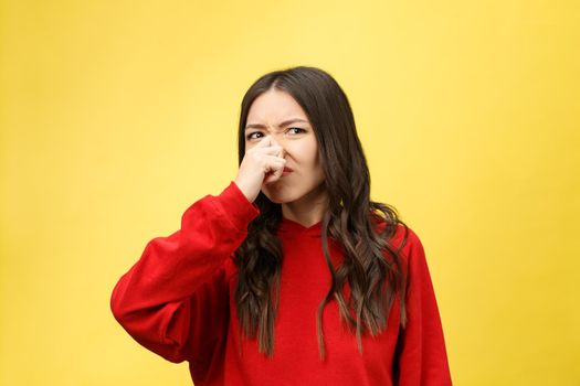 Smell bad. Young lady makes disgusts the smell isolate on yellow background.