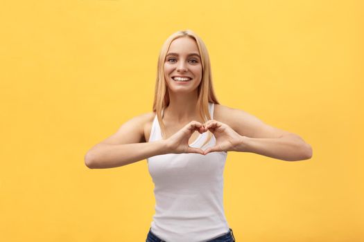 Beautiful Woman Making Heart Shape Sign against a yellow background