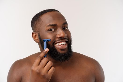 Close up of a happy naked african man shaving with razor isolated over gray background