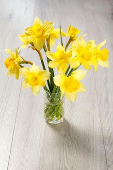 Bouquet of yellow daffodils in vase on wooden desk