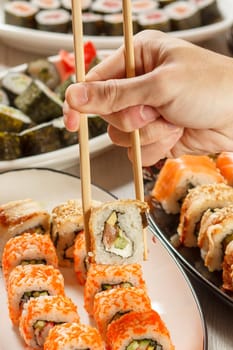 Male hand with two chopsticks holding Uramaki sushi roll