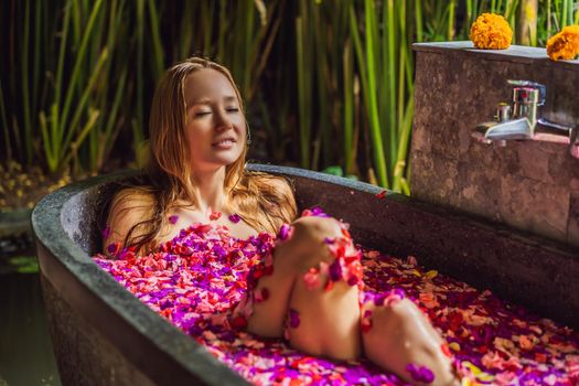 Attractive Young woman in bath with petals of tropical flowers and aroma oils. Spa treatments for skin rejuvenation. Alluring woman in Spa salon. Girl relaxing in bathtub with flower petals. Luxury