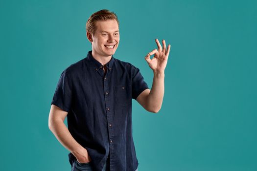Close-up portrait of a ginger guy in navy t-shirt posing on blue background. Sincere emotions.